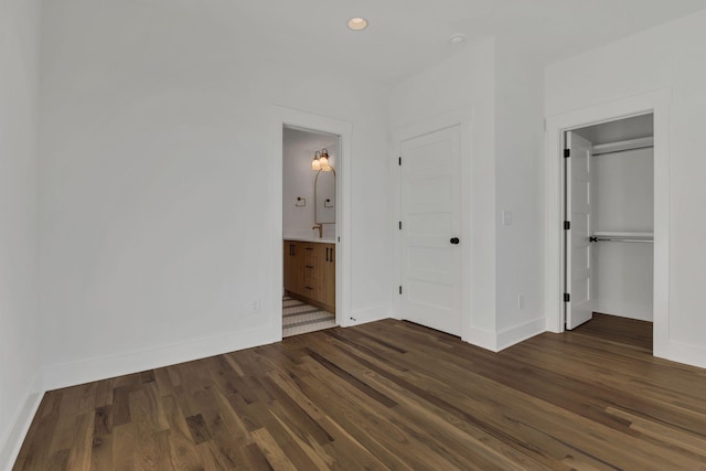 unfurnished bedroom featuring ensuite bath, a closet, and dark wood-type flooring