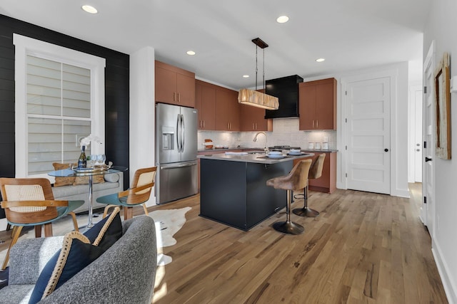 kitchen with stainless steel fridge, light wood-type flooring, a breakfast bar, a center island with sink, and hanging light fixtures