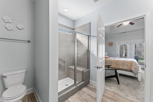 bathroom with ceiling fan, wood-type flooring, toilet, a shower with shower door, and ornamental molding