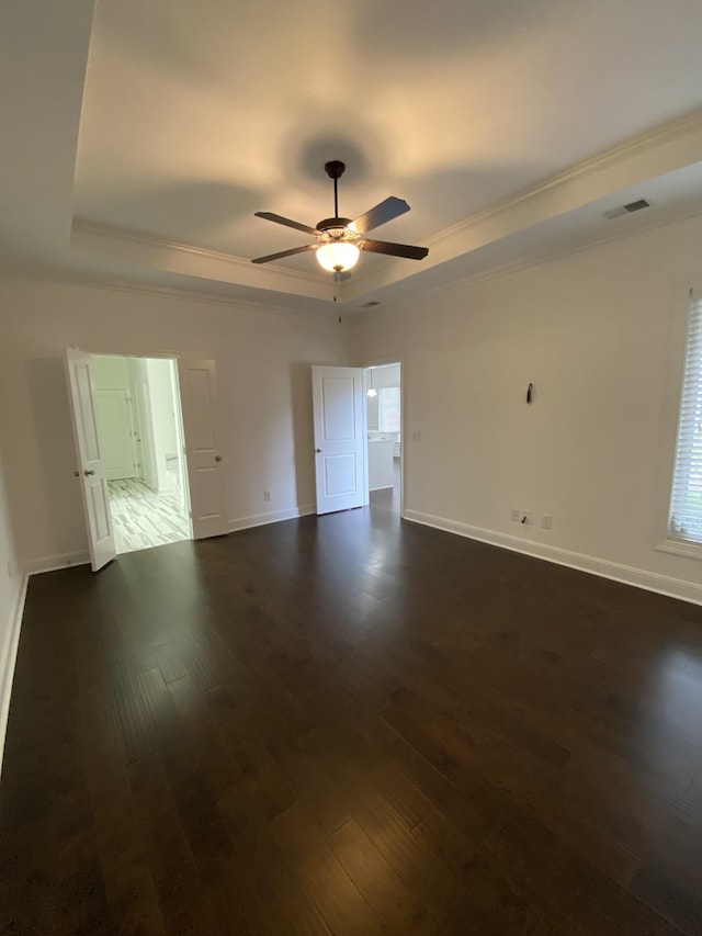 empty room with a raised ceiling, ceiling fan, dark hardwood / wood-style flooring, and ornamental molding