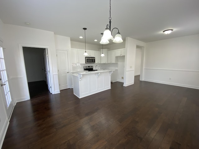 kitchen with appliances with stainless steel finishes, pendant lighting, a center island with sink, dark hardwood / wood-style floors, and white cabinetry