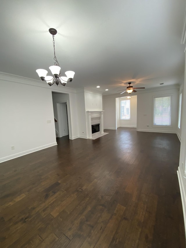 unfurnished living room with ceiling fan with notable chandelier, crown molding, and dark wood-type flooring