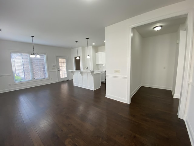 unfurnished living room featuring a notable chandelier, dark hardwood / wood-style floors, and a healthy amount of sunlight