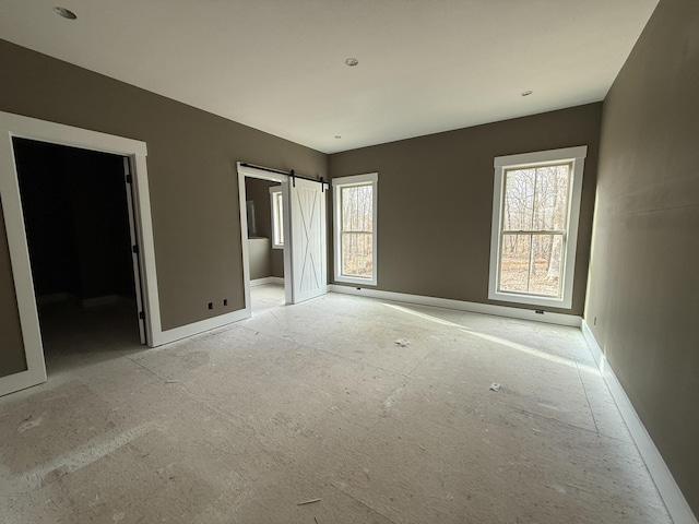 unfurnished bedroom with a barn door, a spacious closet, and multiple windows