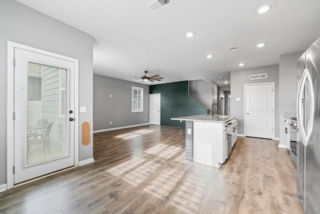 kitchen featuring light wood-type flooring, a kitchen island with sink, ceiling fan, sink, and white cabinets