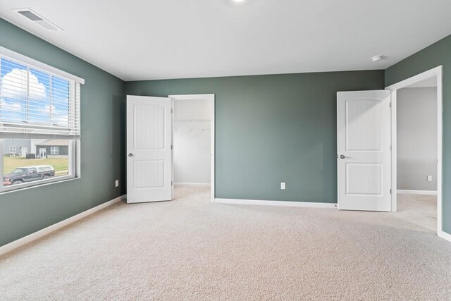 unfurnished bedroom featuring a spacious closet, light carpet, and a closet