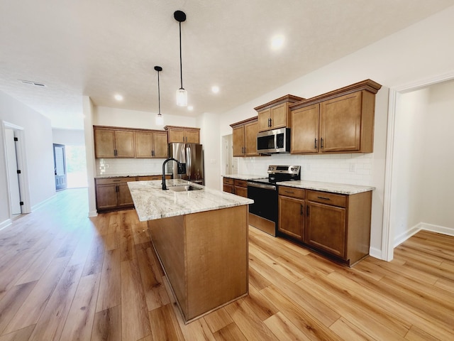 kitchen with stainless steel appliances, sink, pendant lighting, a center island with sink, and light hardwood / wood-style flooring