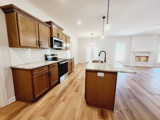 kitchen with light wood-type flooring, stainless steel appliances, sink, a center island with sink, and hanging light fixtures