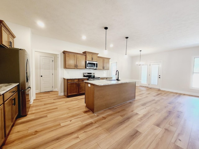 kitchen with pendant lighting, a kitchen island with sink, sink, light wood-type flooring, and appliances with stainless steel finishes