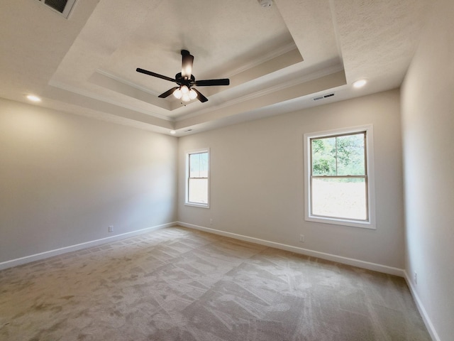 empty room featuring a tray ceiling, crown molding, ceiling fan, and light colored carpet