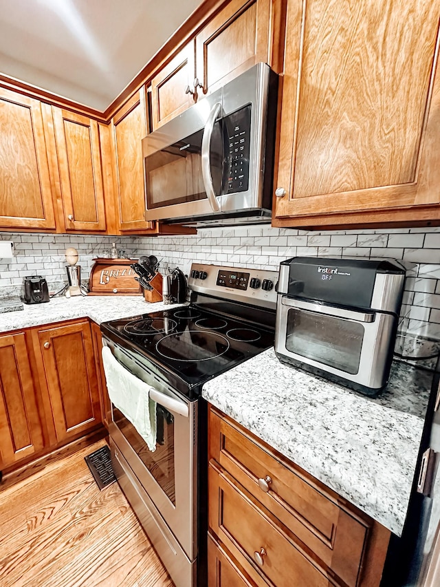 kitchen with tasteful backsplash, light stone counters, stainless steel appliances, and light hardwood / wood-style floors