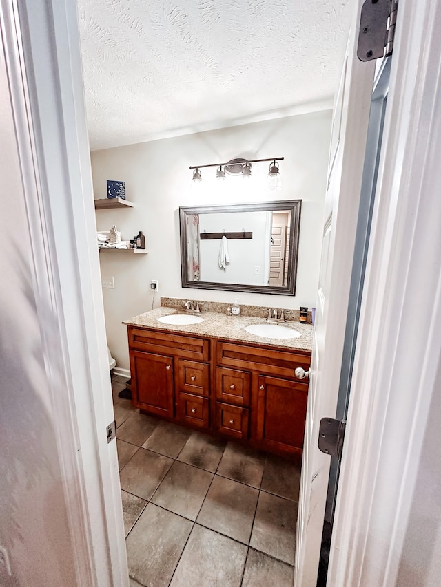 bathroom with toilet, a textured ceiling, vanity, and tile patterned floors