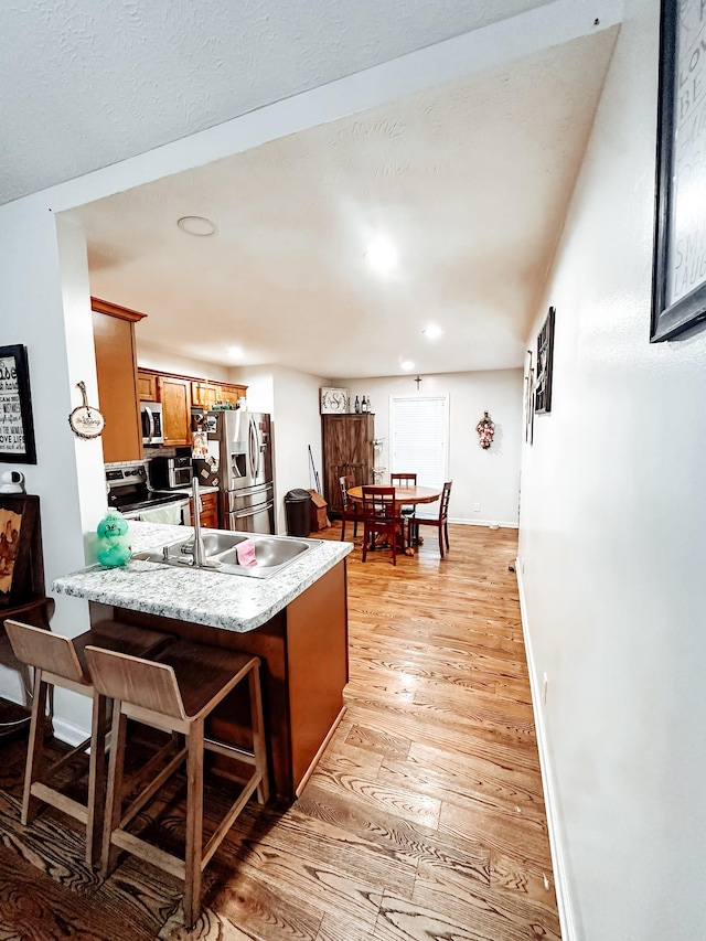 kitchen with sink, a breakfast bar area, light hardwood / wood-style flooring, kitchen peninsula, and stainless steel appliances