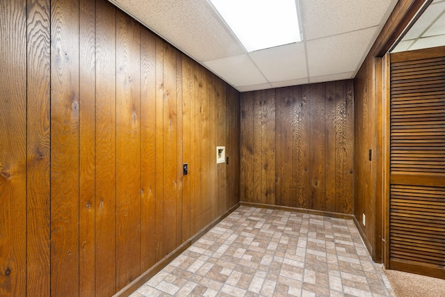 empty room featuring a drop ceiling and wood walls