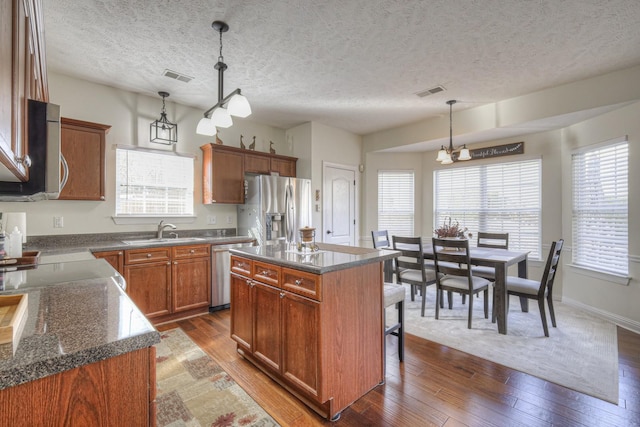 kitchen with stainless steel appliances, dark wood-type flooring, a healthy amount of sunlight, decorative light fixtures, and a center island