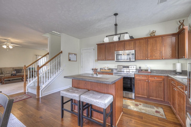 kitchen with appliances with stainless steel finishes, a textured ceiling, ceiling fan, dark wood-type flooring, and a kitchen island