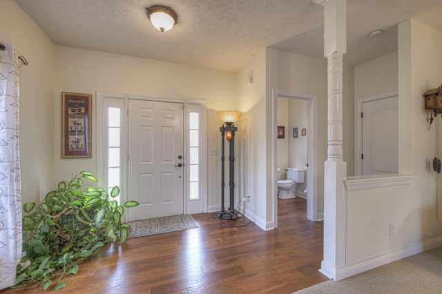 foyer entrance with a textured ceiling, ornate columns, a healthy amount of sunlight, and dark hardwood / wood-style floors