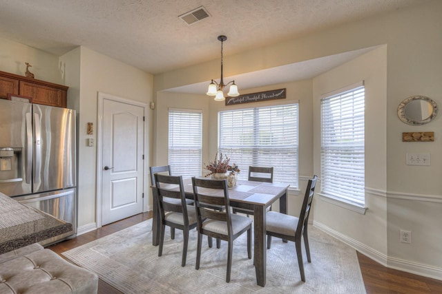 dining area featuring a textured ceiling, a notable chandelier, and dark wood-type flooring