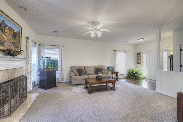 carpeted living room featuring a fireplace, a textured ceiling, decorative columns, and ceiling fan