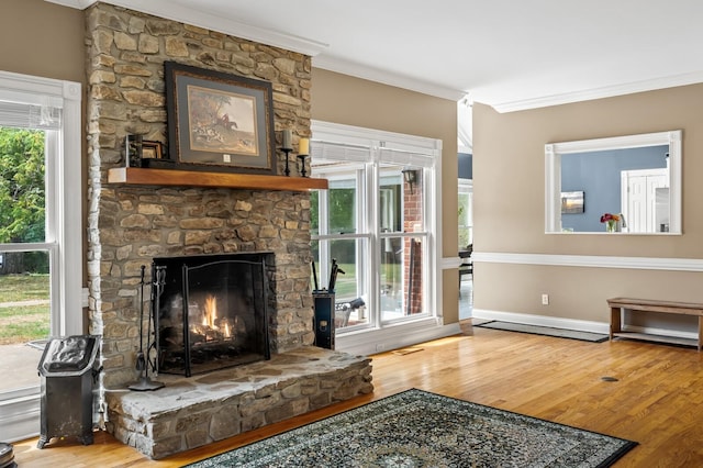 living room with hardwood / wood-style flooring, a stone fireplace, a wealth of natural light, and crown molding