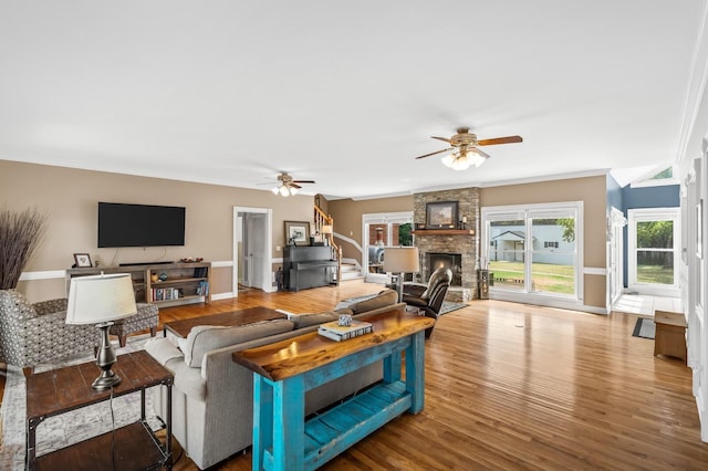 living room with hardwood / wood-style flooring, a stone fireplace, ceiling fan, and ornamental molding