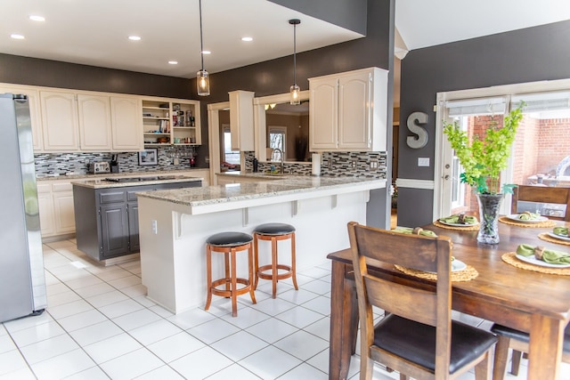 kitchen with light stone countertops, a kitchen breakfast bar, tasteful backsplash, stainless steel fridge, and decorative light fixtures