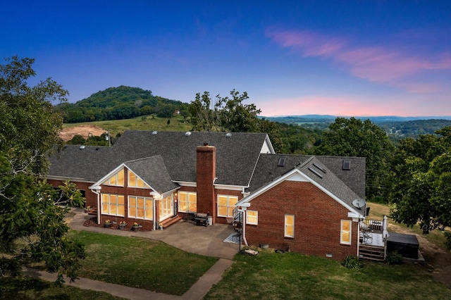 back house at dusk with a yard, a sunroom, a patio, and a mountain view