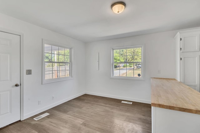 interior space with baseboards, wood finished floors, visible vents, and a healthy amount of sunlight