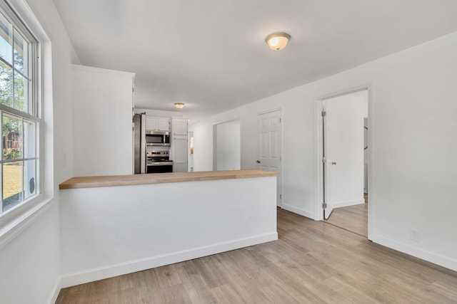 kitchen with appliances with stainless steel finishes, light wood-type flooring, white cabinets, and a peninsula