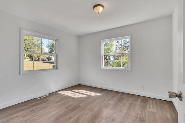 unfurnished room featuring baseboards, visible vents, and wood finished floors