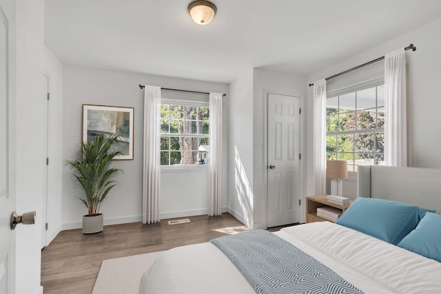 bedroom featuring baseboards, multiple windows, visible vents, and wood finished floors