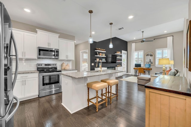 kitchen featuring white cabinets, an island with sink, decorative light fixtures, and appliances with stainless steel finishes