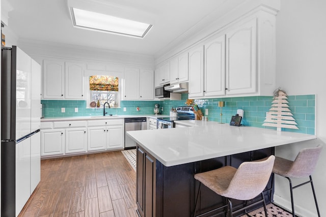 kitchen featuring a kitchen bar, appliances with stainless steel finishes, kitchen peninsula, sink, and white cabinets