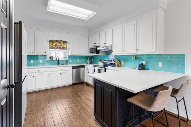 kitchen featuring appliances with stainless steel finishes, dark hardwood / wood-style floors, sink, white cabinets, and a kitchen breakfast bar