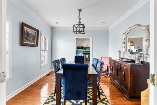 dining area with crown molding, an inviting chandelier, and light hardwood / wood-style floors