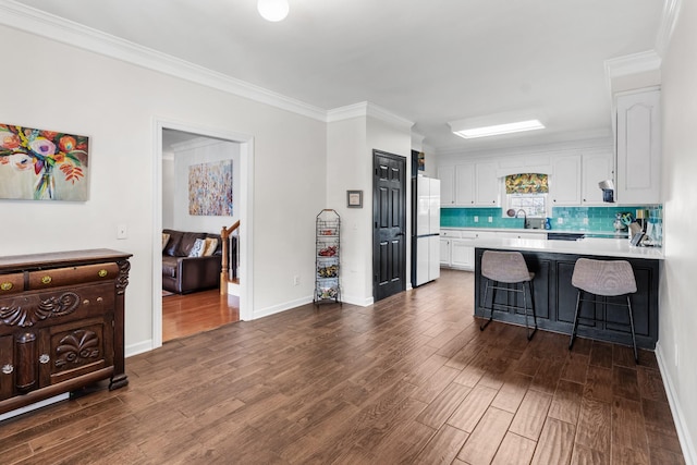 kitchen featuring a kitchen bar, dark hardwood / wood-style floors, white fridge, decorative backsplash, and white cabinets