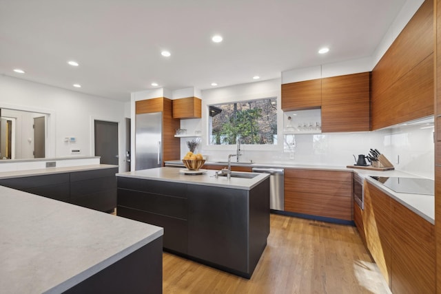 kitchen featuring sink, a kitchen island with sink, stainless steel appliances, light hardwood / wood-style floors, and decorative backsplash