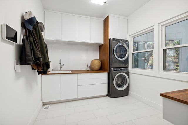 clothes washing area featuring stacked washer / drying machine, cabinets, light tile patterned floors, and sink