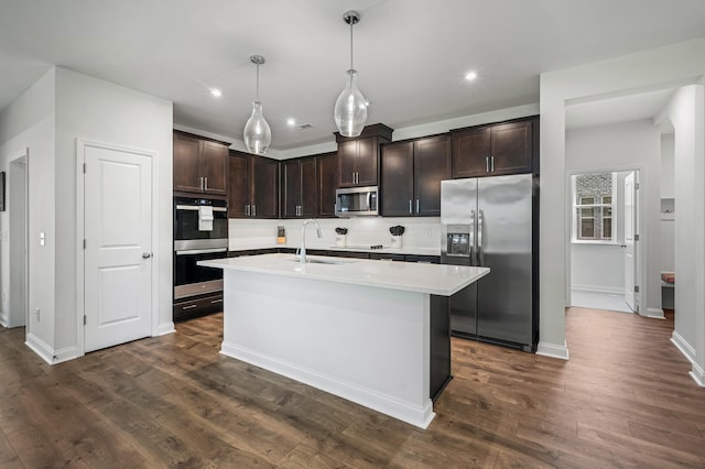 kitchen with a kitchen island with sink, dark wood-type flooring, sink, decorative light fixtures, and stainless steel appliances