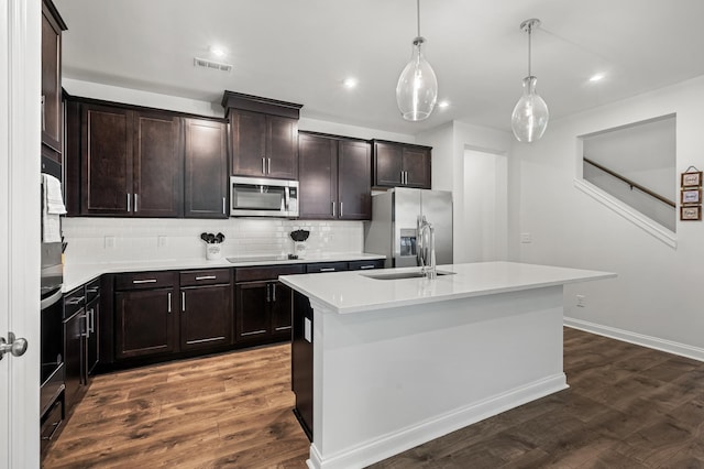 kitchen featuring dark wood-type flooring, a center island with sink, stainless steel appliances, and decorative light fixtures