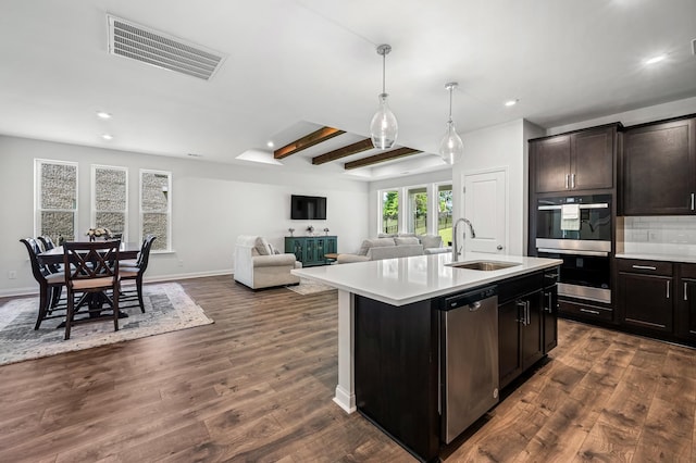 kitchen with sink, beamed ceiling, dark hardwood / wood-style floors, an island with sink, and appliances with stainless steel finishes