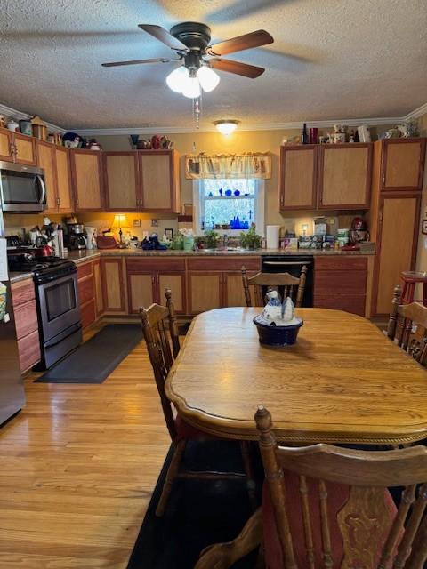 kitchen with light wood-type flooring, a textured ceiling, stainless steel appliances, and ornamental molding