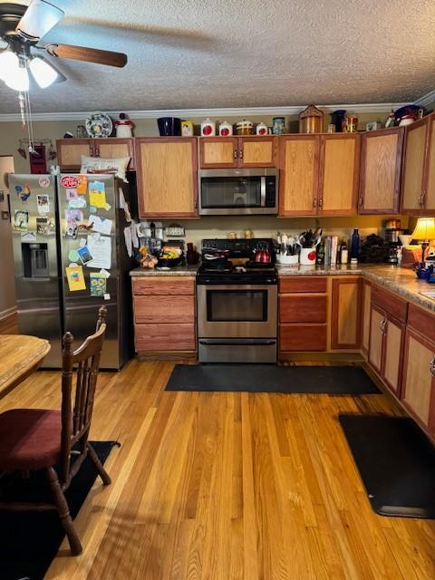 kitchen featuring appliances with stainless steel finishes, a textured ceiling, ceiling fan, crown molding, and light hardwood / wood-style flooring