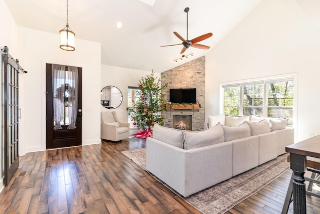 living room with ceiling fan, a stone fireplace, dark hardwood / wood-style flooring, and high vaulted ceiling