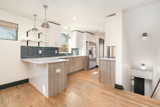 kitchen featuring tasteful backsplash, light hardwood / wood-style flooring, stainless steel fridge, pendant lighting, and white cabinets