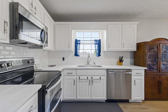 kitchen featuring white cabinetry, sink, stainless steel appliances, light hardwood / wood-style flooring, and decorative backsplash