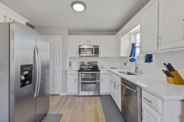 kitchen featuring white cabinetry, sink, stainless steel appliances, and light wood-type flooring