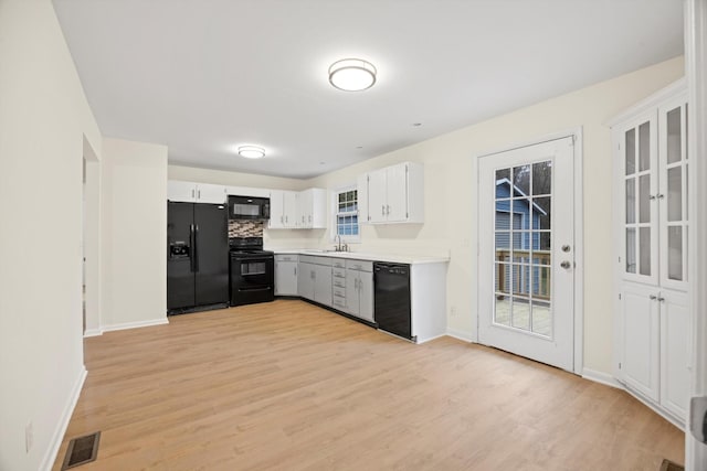 kitchen with sink, backsplash, light hardwood / wood-style floors, white cabinets, and black appliances