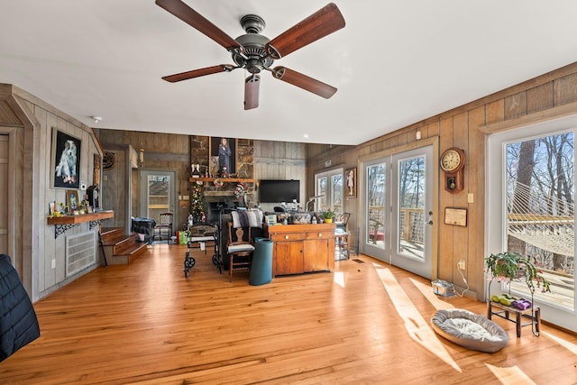 living room featuring a fireplace, light hardwood / wood-style floors, ceiling fan, and wood walls