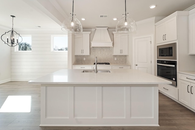 kitchen featuring sink, hanging light fixtures, an island with sink, black appliances, and custom range hood